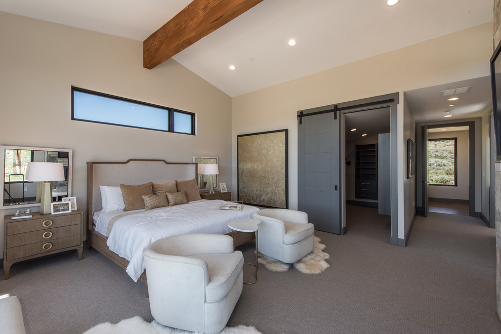 Imagen de dormitorio principal rústico de tamaño medio con paredes beige, moqueta, chimenea lineal, marco de chimenea de piedra y suelo gris