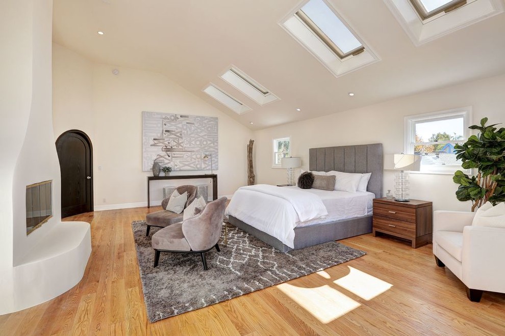 ロサンゼルスにあるトランジショナルスタイルのおしゃれな主寝室 (ベージュの壁、淡色無垢フローリング、横長型暖炉、漆喰の暖炉まわり、ベージュの床、グレーとブラウン)