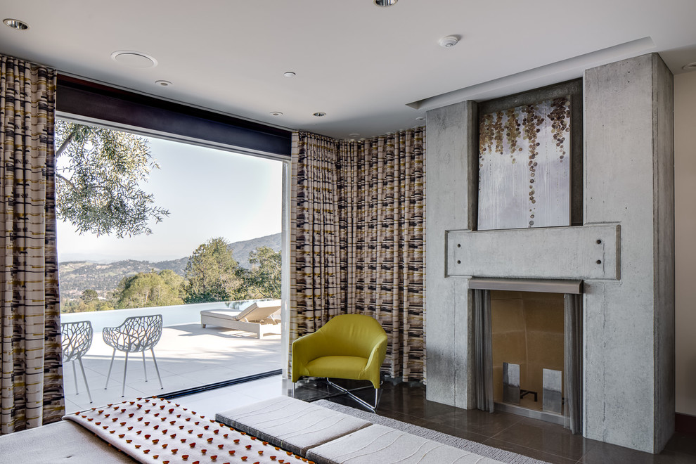 На фото: большая хозяйская спальня в стиле модернизм с белыми стенами, полом из известняка, стандартным камином, фасадом камина из бетона и коричневым полом