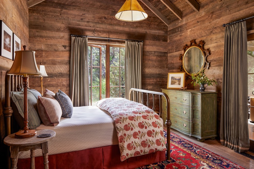 Modelo de dormitorio rural sin chimenea con paredes marrones y suelo de madera en tonos medios