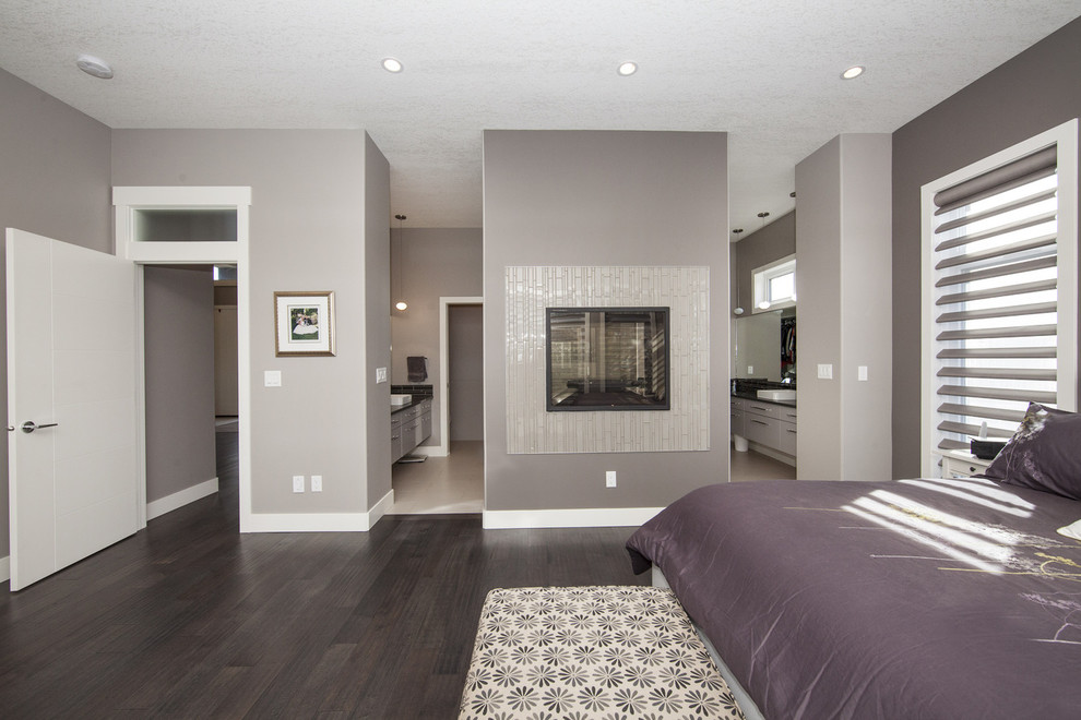 Large contemporary master bedroom in Edmonton with grey walls, dark hardwood flooring, a tiled fireplace surround and a two-sided fireplace.