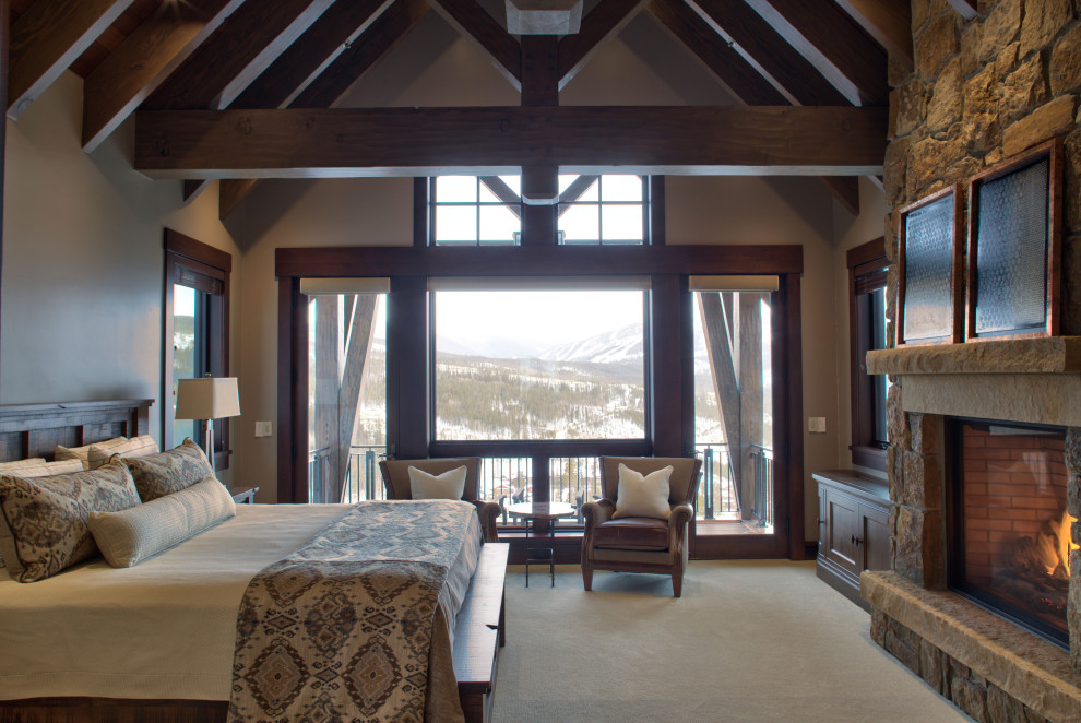 Example of a mountain style master carpeted, beige floor, exposed beam and vaulted ceiling bedroom design in Denver with beige walls, a standard fireplace and a stone fireplace