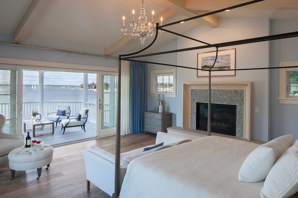 Modelo de dormitorio tipo loft costero extra grande con paredes azules, suelo de madera clara, todas las chimeneas, marco de chimenea de baldosas y/o azulejos y suelo marrón