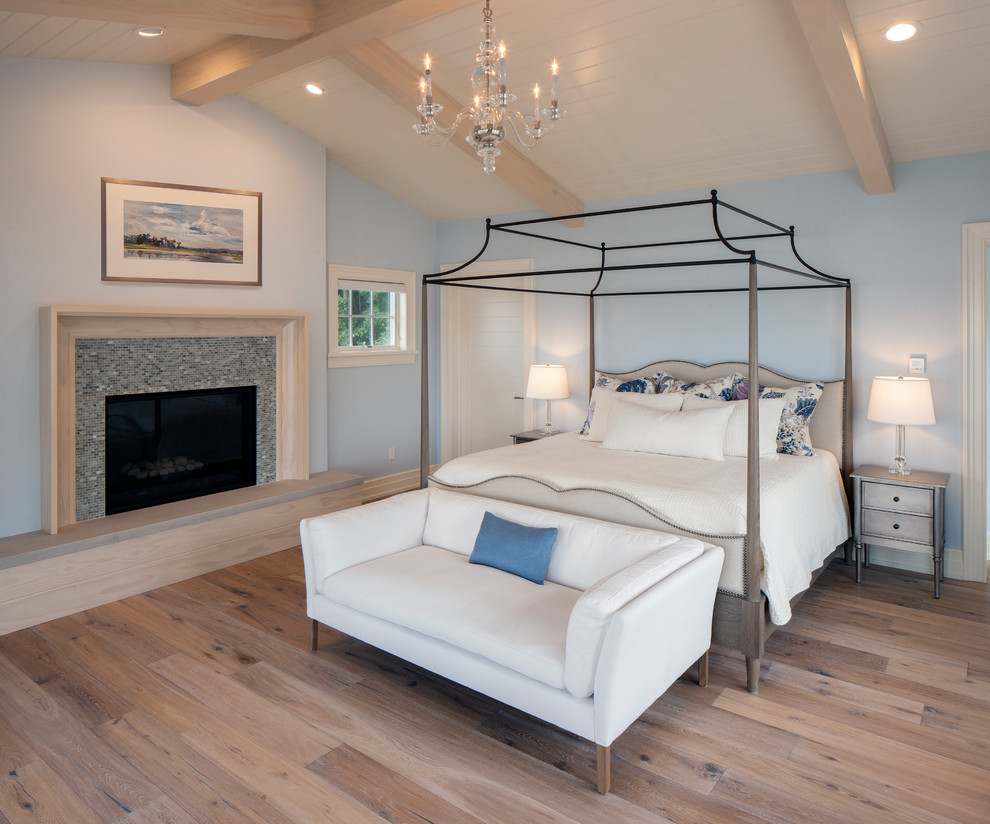 На фото: огромная спальня на антресоли в морском стиле с синими стенами, светлым паркетным полом, стандартным камином, фасадом камина из плитки и коричневым полом