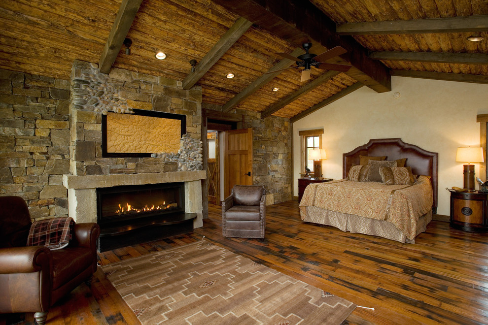 Großes Rustikales Hauptschlafzimmer mit braunem Holzboden, Kaminumrandung aus Stein und braunem Boden in Sonstige