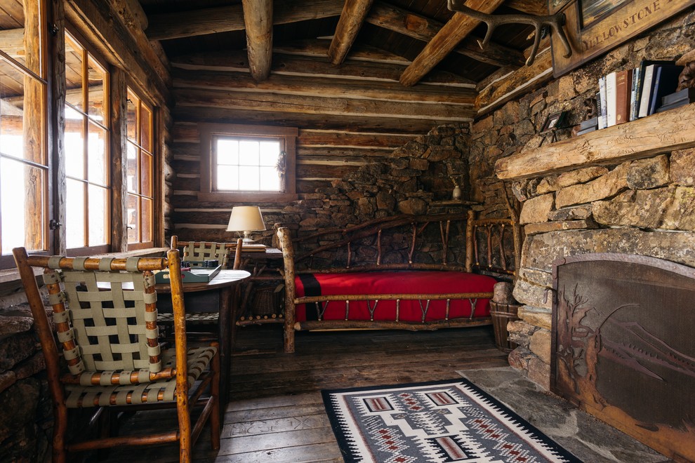 Photo of a small rustic bedroom in Other with brown walls, dark hardwood flooring, a standard fireplace and a stone fireplace surround.