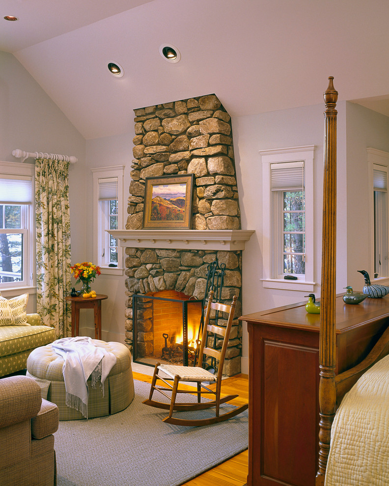Ejemplo de dormitorio principal de estilo americano grande con paredes blancas, suelo de madera oscura, todas las chimeneas y marco de chimenea de piedra
