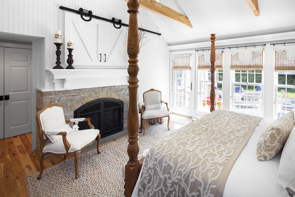 Example of a large beach style master dark wood floor and brown floor bedroom design in Boston with white walls, a standard fireplace and a stone fireplace