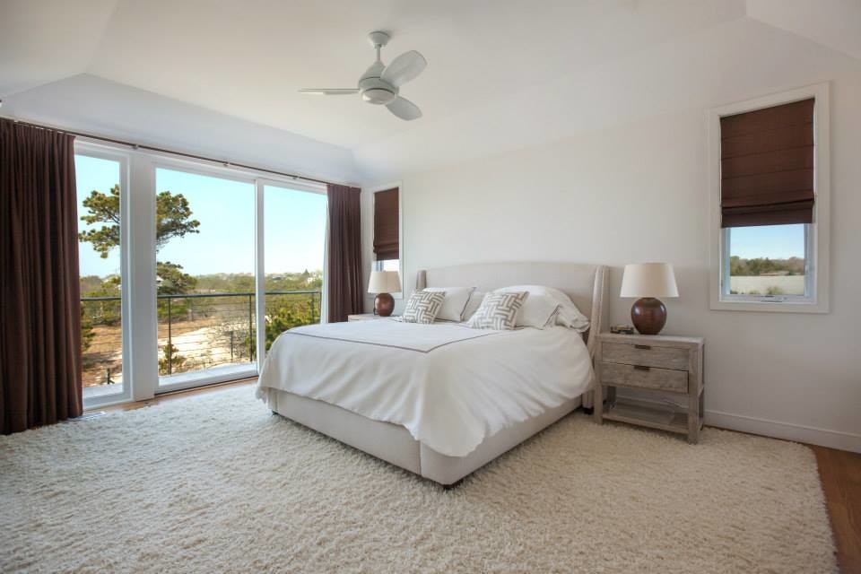 Modelo de dormitorio principal costero de tamaño medio con paredes blancas y suelo de madera en tonos medios