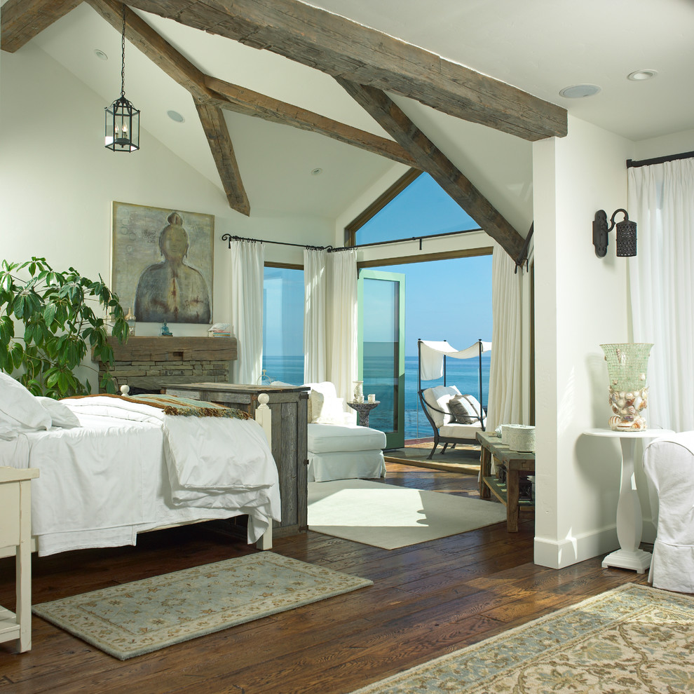 На фото: большая хозяйская спальня в морском стиле с темным паркетным полом, стандартным камином, фасадом камина из камня, коричневым полом и белыми стенами с
