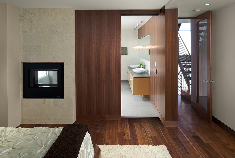 На фото: спальня в стиле модернизм с фасадом камина из камня и двусторонним камином с