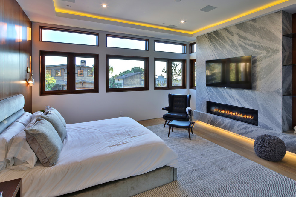 Источник вдохновения для домашнего уюта: хозяйская спальня в стиле модернизм с белыми стенами, светлым паркетным полом, горизонтальным камином и фасадом камина из камня