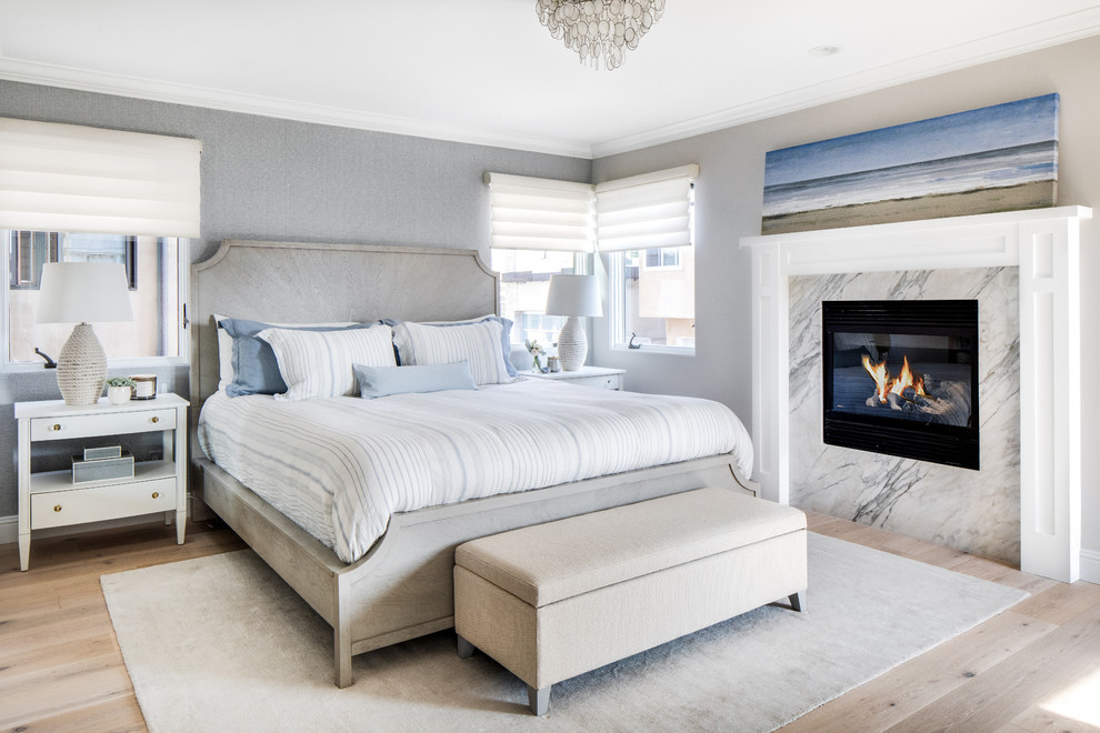 Inspiration for a medium sized beach style master bedroom in Los Angeles with grey walls, light hardwood flooring, a standard fireplace, a stone fireplace surround and beige floors.