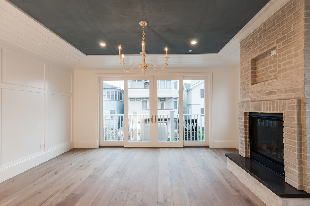 Cette photo montre une grande chambre parentale nature avec un mur blanc, parquet clair, une cheminée standard, un manteau de cheminée en brique et un sol marron.