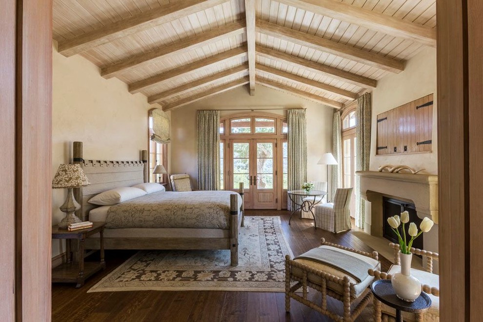 Inspiration for a country bedroom in San Francisco with beige walls, dark hardwood flooring, a standard fireplace, a stone fireplace surround and feature lighting.