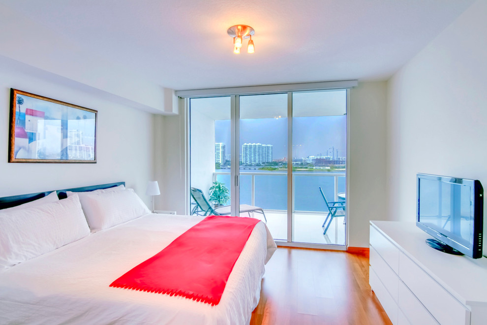 Modelo de dormitorio principal tropical de tamaño medio con paredes blancas y suelo de madera clara
