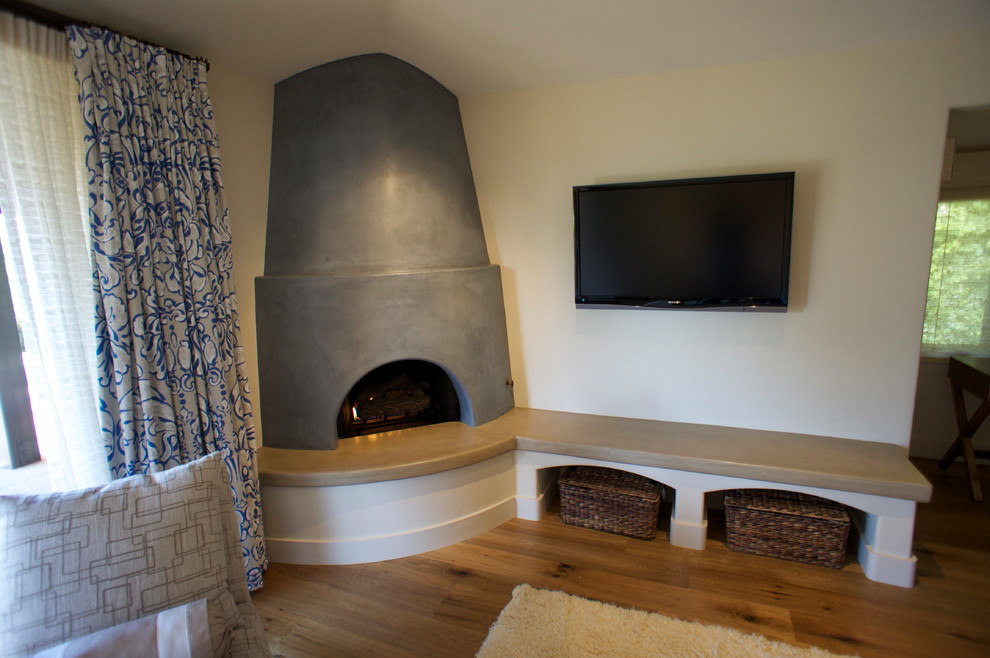 Imagen de dormitorio principal tradicional renovado de tamaño medio con paredes beige, suelo de madera en tonos medios, chimenea de esquina y marco de chimenea de hormigón
