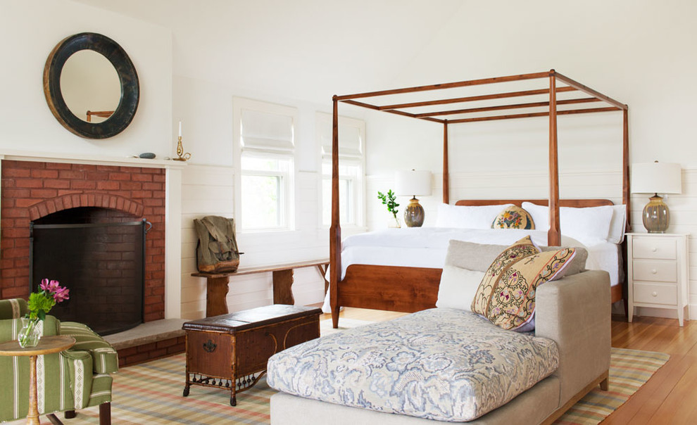 Foto de dormitorio principal marinero grande con paredes blancas, suelo de madera en tonos medios, todas las chimeneas y marco de chimenea de ladrillo