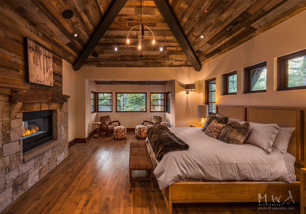 Foto de dormitorio principal contemporáneo grande con paredes beige, suelo de madera en tonos medios, chimenea de doble cara, marco de chimenea de piedra y suelo marrón