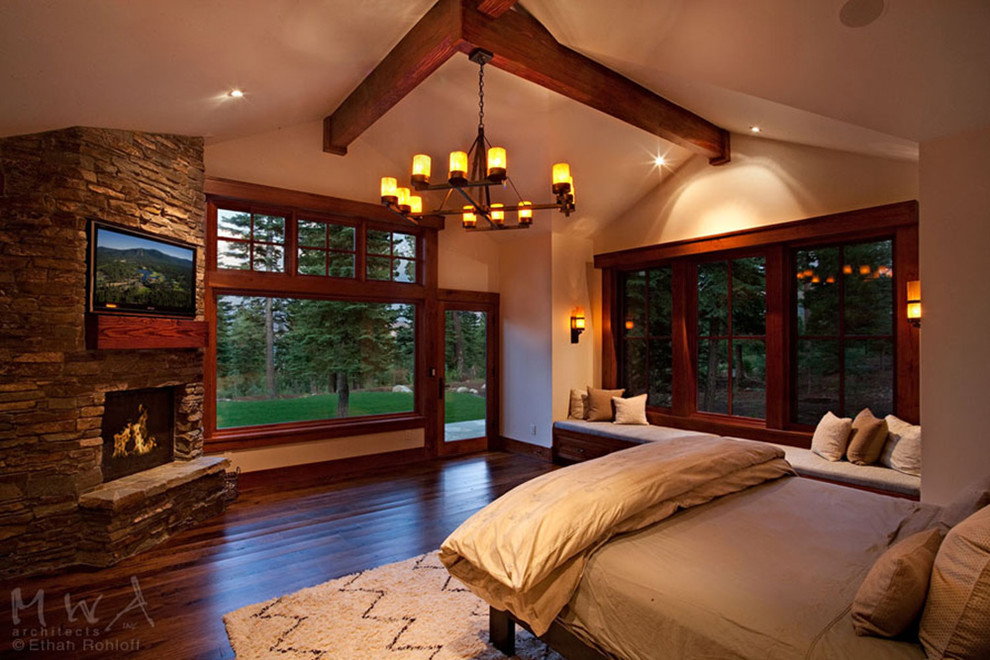 Imagen de dormitorio principal de estilo americano grande con paredes beige, suelo de madera oscura, chimenea de esquina y marco de chimenea de piedra