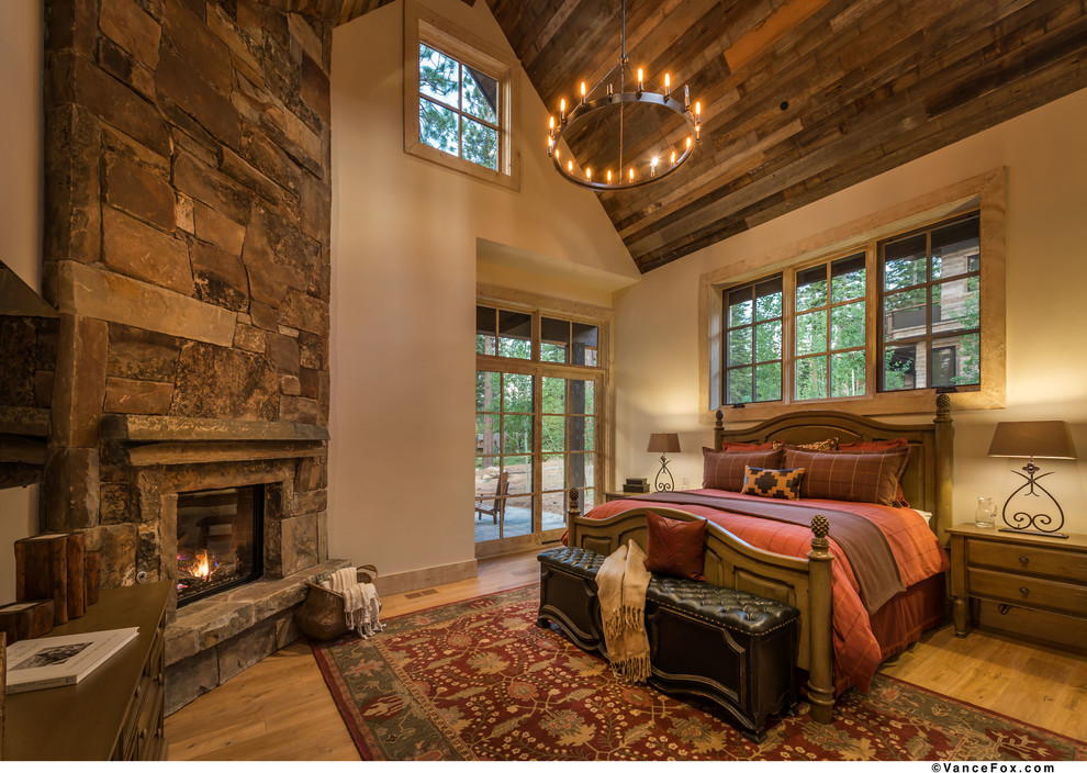 Photo of a medium sized rustic master bedroom in Sacramento with light hardwood flooring, beige walls, a standard fireplace, a stone fireplace surround and feature lighting.
