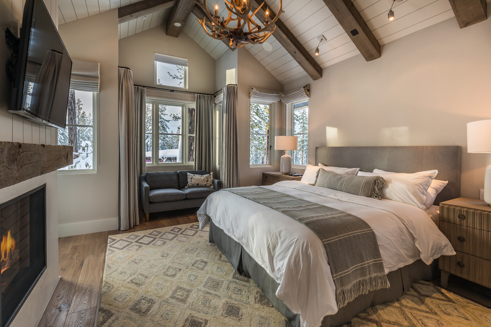 Réalisation d'une chambre parentale chalet de taille moyenne avec un mur beige, un sol en bois brun, une cheminée standard, un manteau de cheminée en pierre et un sol marron.