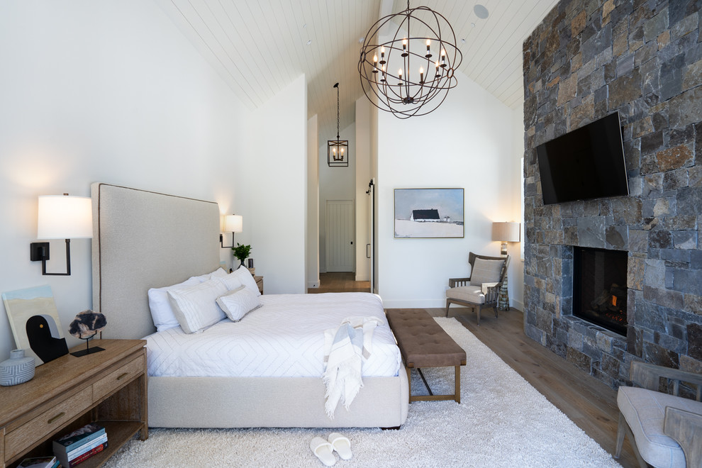Landhausstil Hauptschlafzimmer mit weißer Wandfarbe, Kamin, Kaminumrandung aus Stein, dunklem Holzboden und braunem Boden in Sonstige