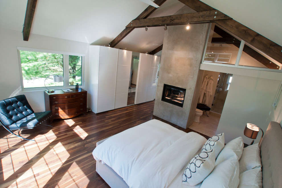 Foto de dormitorio principal minimalista de tamaño medio con paredes blancas, suelo de madera en tonos medios, chimenea de doble cara, marco de chimenea de hormigón y suelo marrón