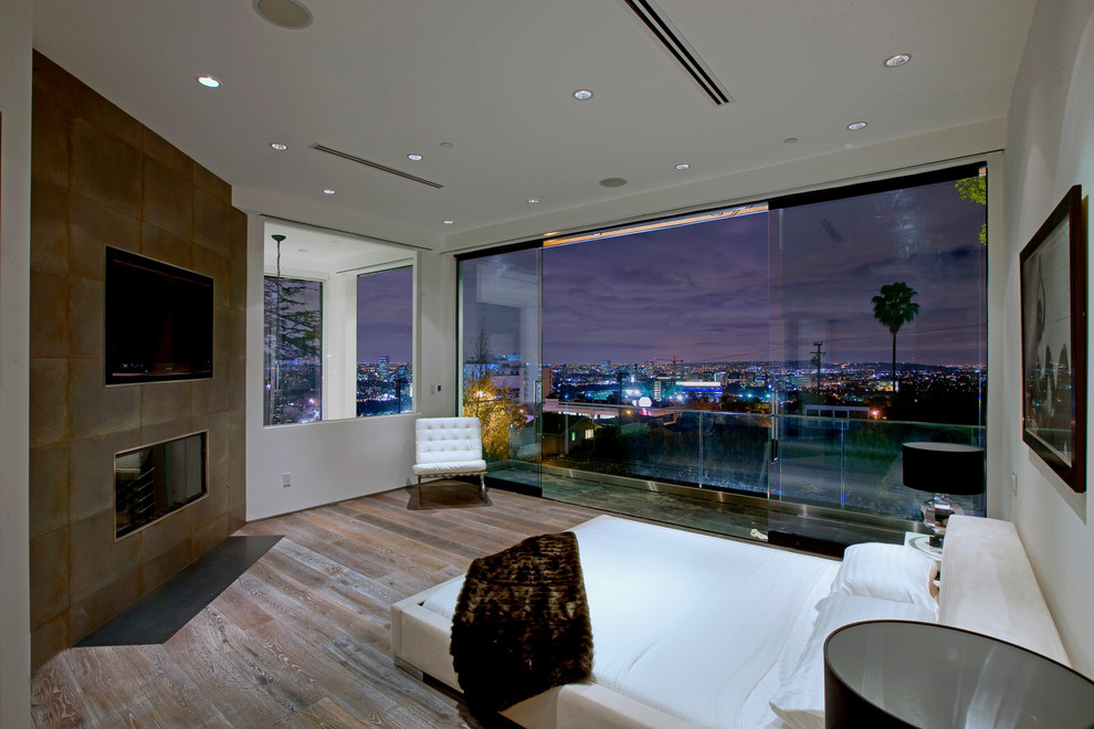 Großes Modernes Hauptschlafzimmer mit weißer Wandfarbe, braunem Holzboden, Kaminumrandung aus Metall und Eckkamin in Los Angeles