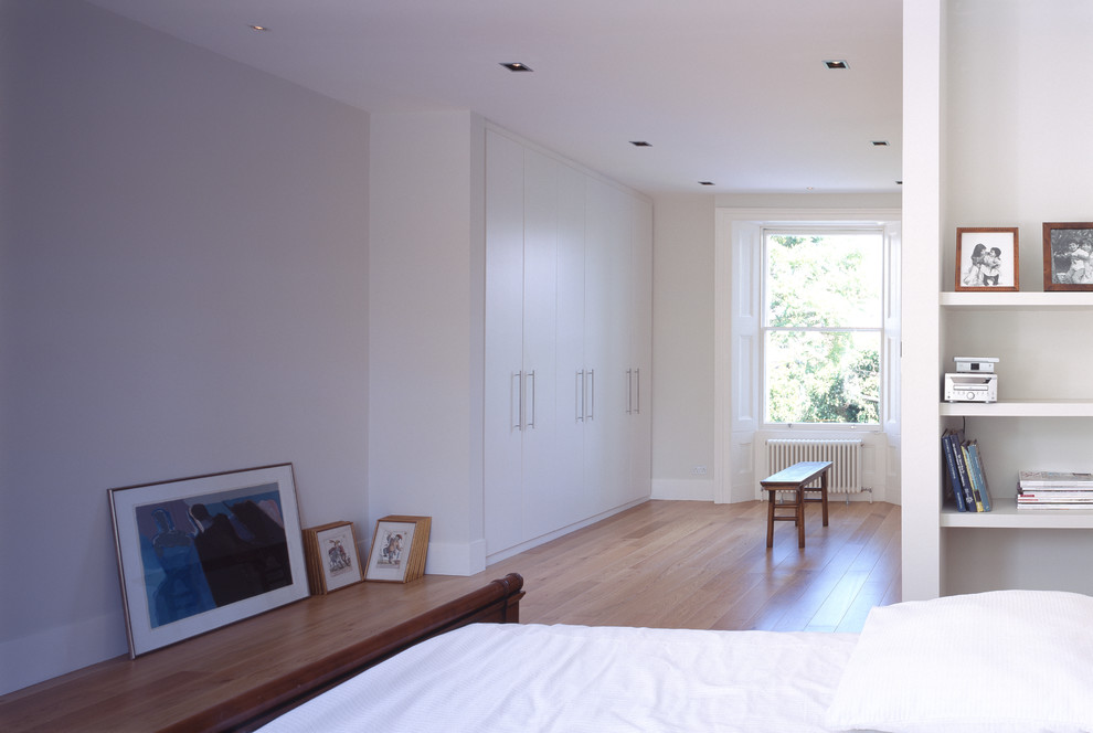 This is an example of a large modern master bedroom in London with white walls and medium hardwood flooring.