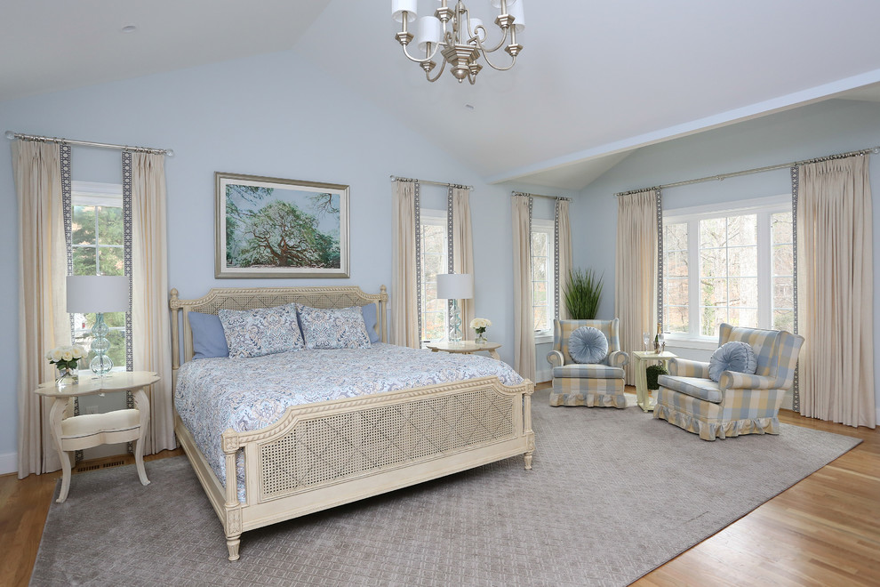 ローリーにある広いトラディショナルスタイルのおしゃれな主寝室 (青い壁、淡色無垢フローリング、標準型暖炉、木材の暖炉まわり、茶色い床、三角天井) のインテリア