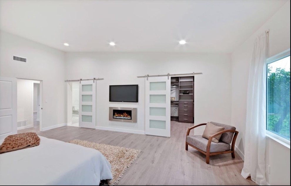 Imagen de dormitorio principal actual grande con paredes blancas, suelo de madera clara, todas las chimeneas, marco de chimenea de metal y suelo beige