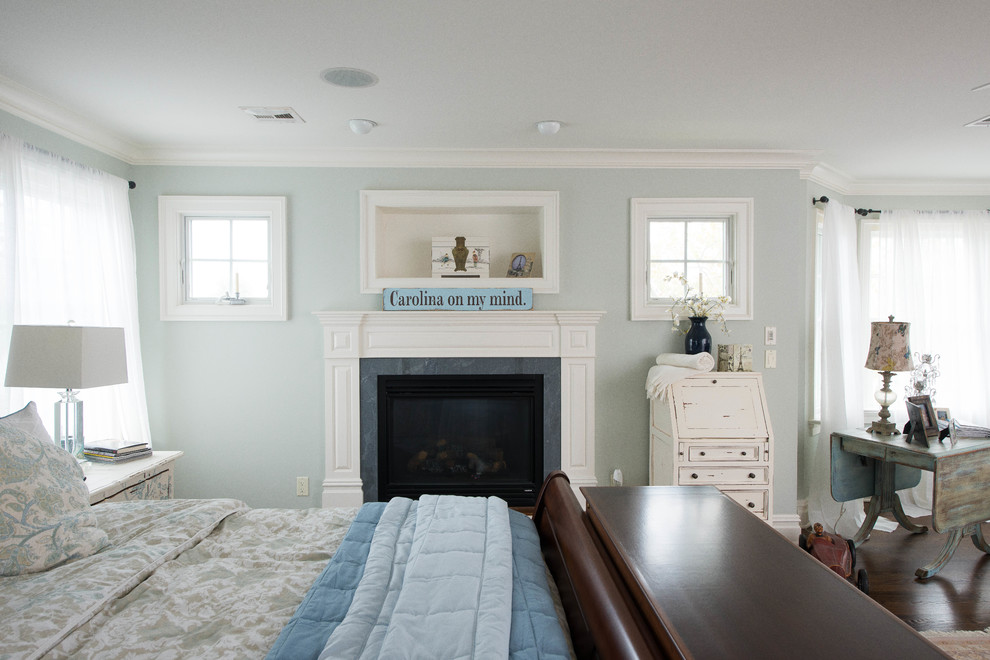 Ejemplo de dormitorio principal costero grande con paredes azules, suelo de madera oscura, todas las chimeneas y marco de chimenea de piedra