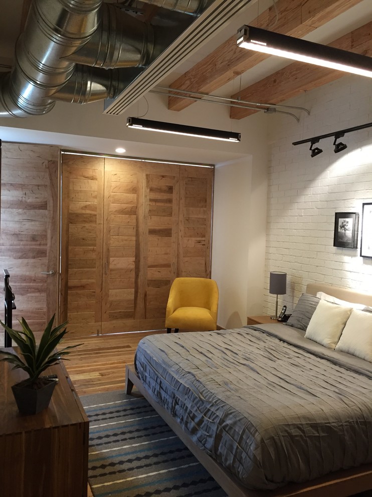 Modelo de dormitorio principal industrial grande con paredes blancas, suelo de madera en tonos medios y suelo marrón