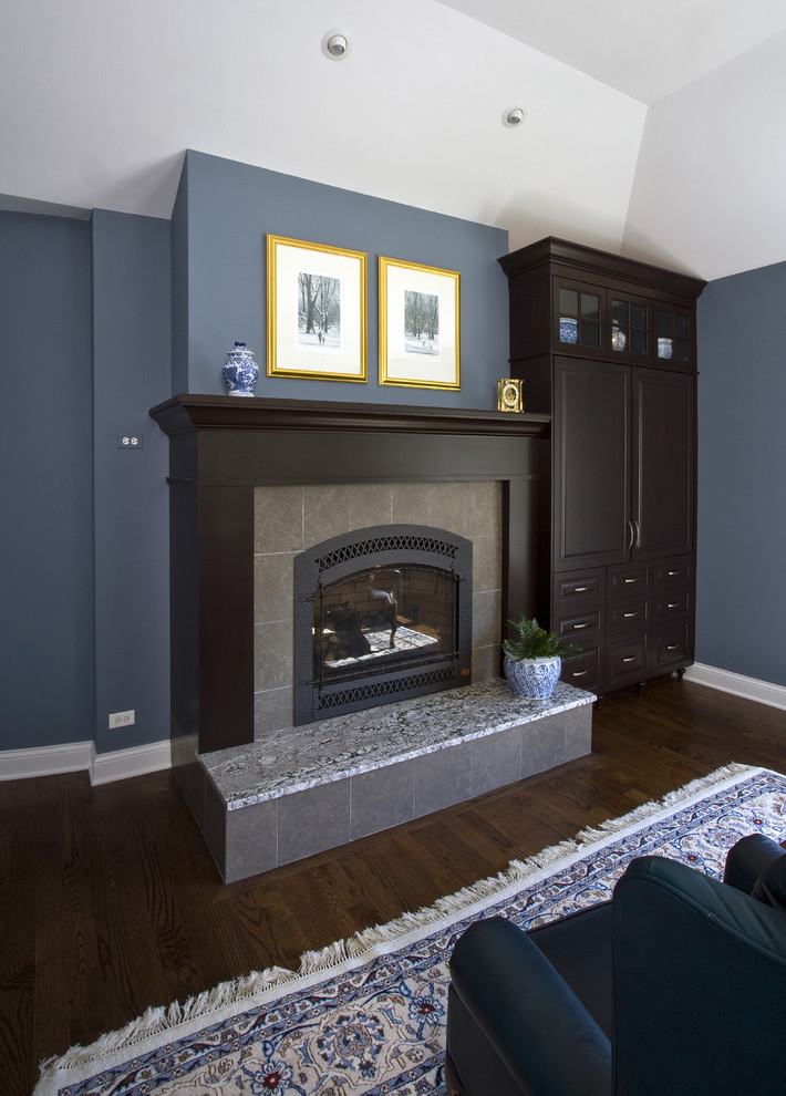 Cette image montre une grande chambre parentale traditionnelle avec un mur bleu, parquet foncé, une cheminée standard, un manteau de cheminée en carrelage, un sol marron et un plafond voûté.
