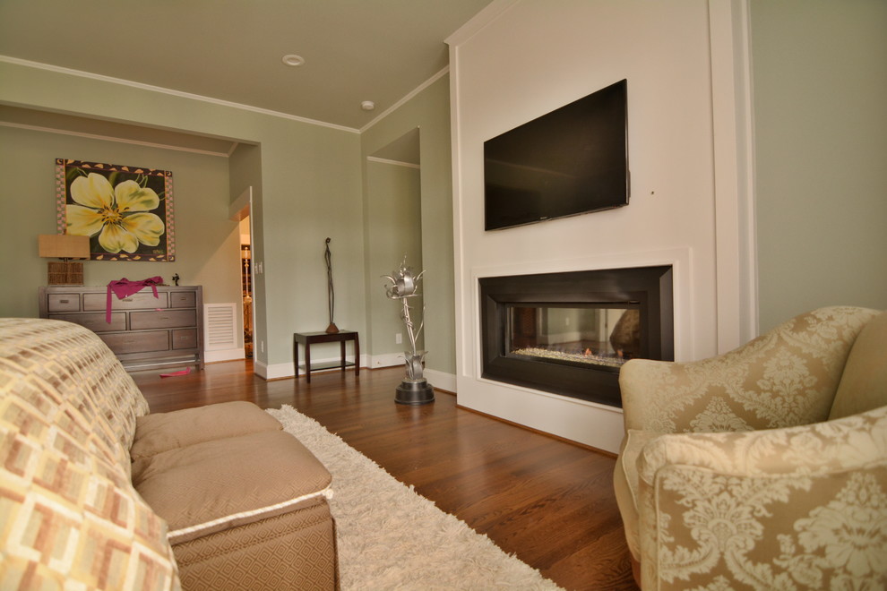 Cette photo montre une très grande chambre parentale tendance avec un mur vert, un sol en bois brun, une cheminée ribbon et un manteau de cheminée en bois.