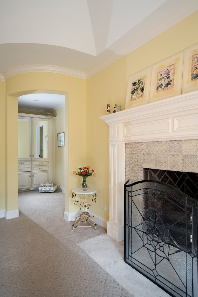 Стильный дизайн: большая хозяйская спальня в классическом стиле с ковровым покрытием, стандартным камином, фасадом камина из плитки и желтыми стенами - последний тренд
