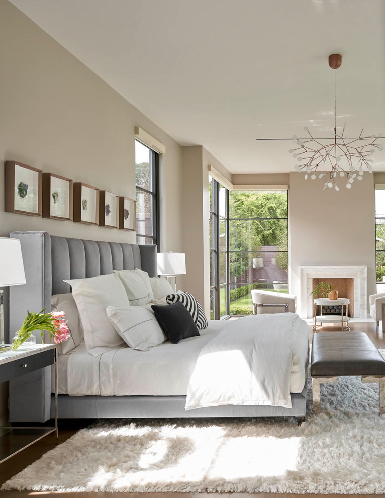 Immagine di una camera da letto contemporanea con pareti beige, pavimento in legno massello medio, camino classico e pavimento marrone