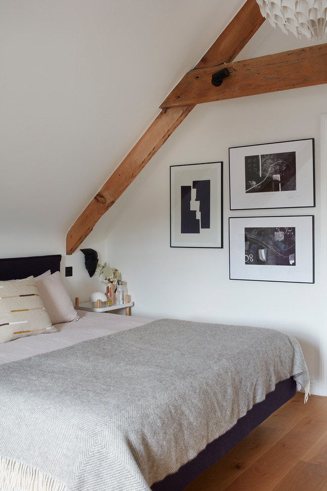 This is an example of a large scandi master bedroom in Devon with white walls, light hardwood flooring, no fireplace and brown floors.