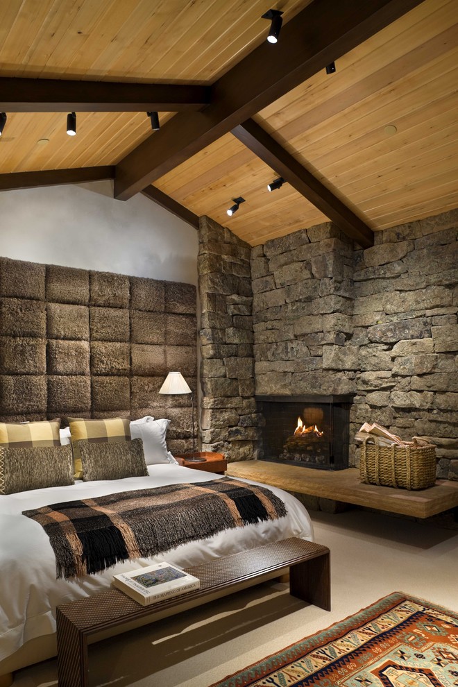 На фото: хозяйская спальня среднего размера в стиле рустика с фасадом камина из камня, угловым камином, белыми стенами и бетонным полом