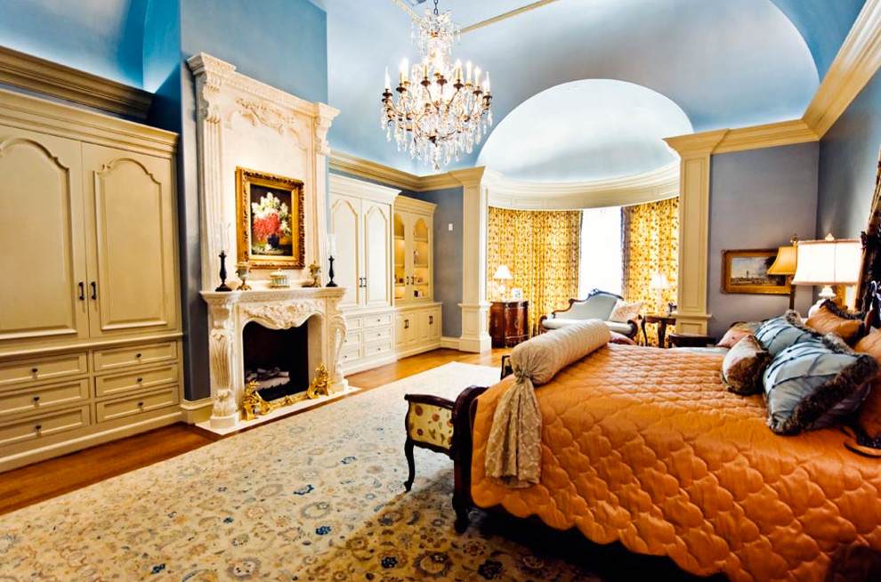 Imagen de dormitorio principal tradicional grande con paredes azules, suelo de madera en tonos medios, todas las chimeneas y marco de chimenea de piedra