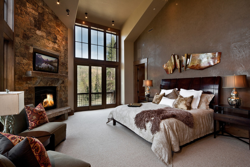 Стильный дизайн: спальня в стиле рустика с угловым камином, фасадом камина из камня и телевизором - последний тренд