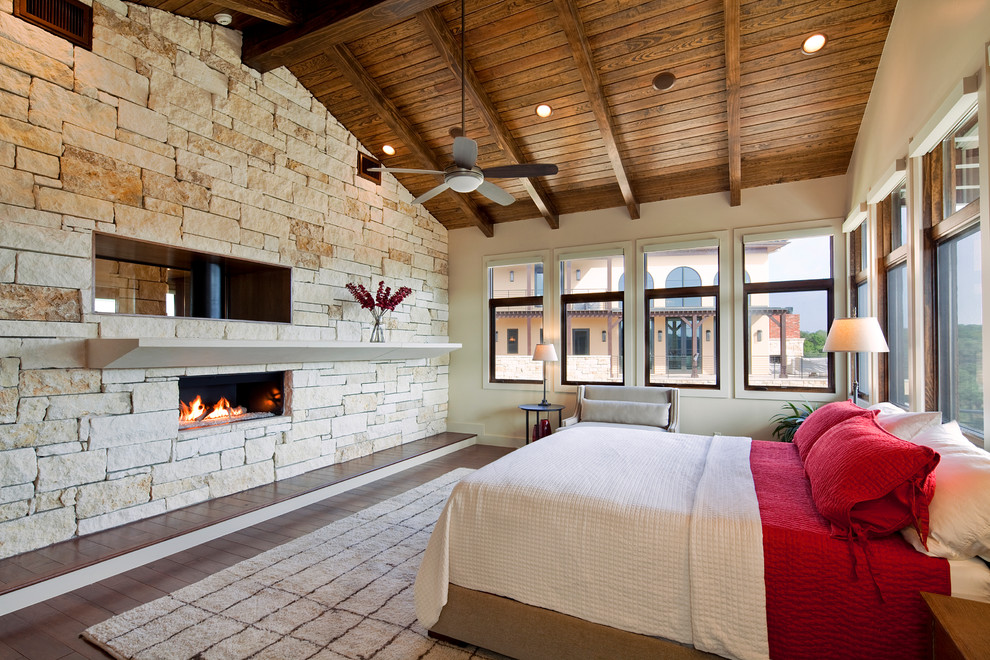 Mediterranes Schlafzimmer mit beiger Wandfarbe, dunklem Holzboden, Gaskamin und Kaminumrandung aus Stein in Austin