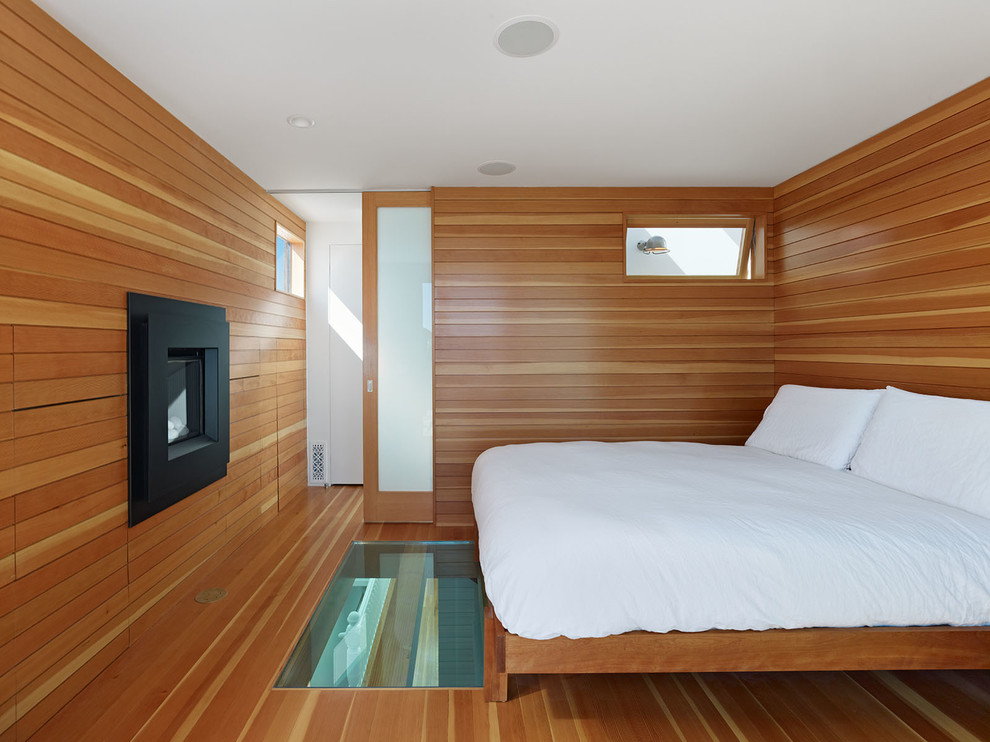 Exemple d'une petite chambre parentale tendance avec une cheminée ribbon, un sol en bois brun et un manteau de cheminée en bois.