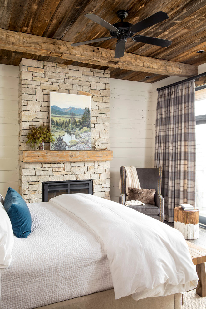 На фото: хозяйская спальня среднего размера в стиле рустика с белыми стенами, темным паркетным полом, стандартным камином, фасадом камина из камня и коричневым полом
