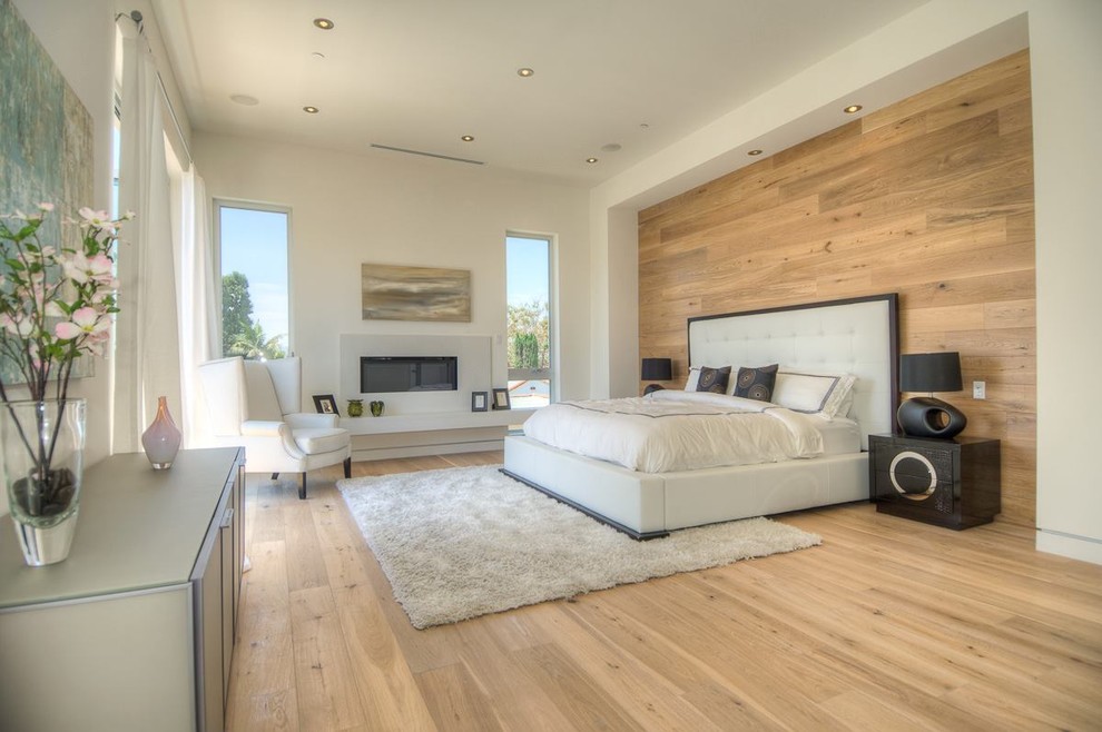 Geräumiges Modernes Hauptschlafzimmer mit weißer Wandfarbe, hellem Holzboden, Gaskamin, Kaminumrandung aus Beton und braunem Boden in Los Angeles