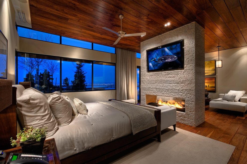 Inspiration pour une chambre design avec un mur beige, un sol en bois brun, un manteau de cheminée en pierre et une cheminée double-face.