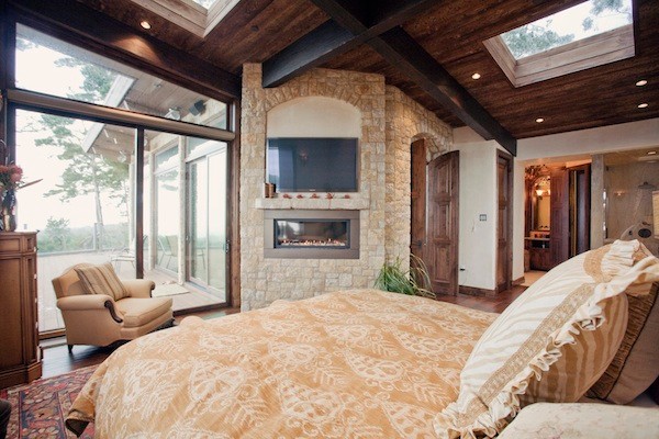 Diseño de dormitorio principal de estilo americano de tamaño medio con paredes beige, suelo de madera en tonos medios, chimenea lineal y marco de chimenea de piedra