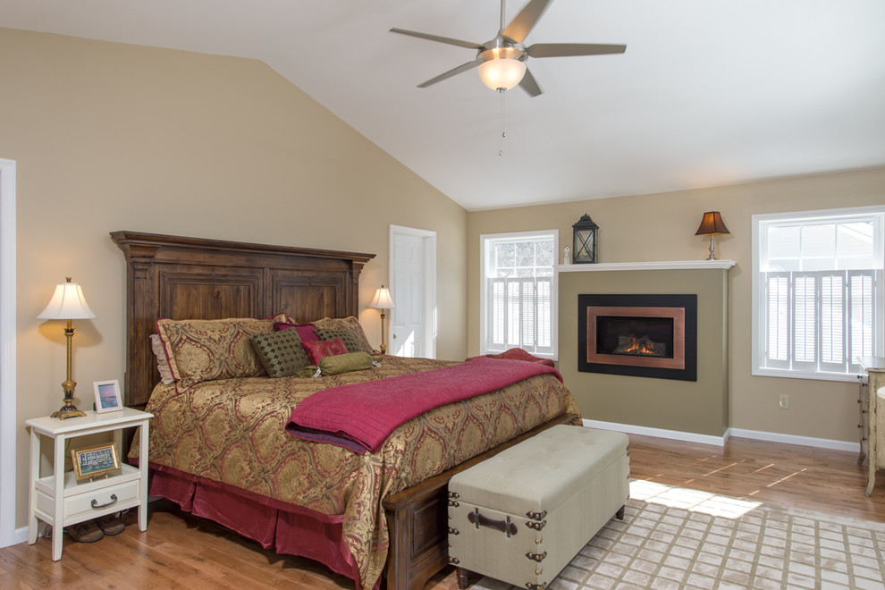 Ejemplo de dormitorio principal de estilo americano de tamaño medio con paredes beige, suelo de madera en tonos medios, todas las chimeneas y marco de chimenea de metal