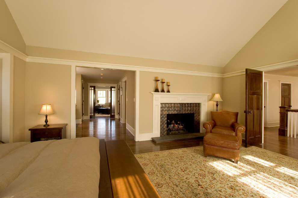 Aménagement d'une grande chambre parentale craftsman avec un mur beige, un sol en bois brun, une cheminée standard et un manteau de cheminée en métal.